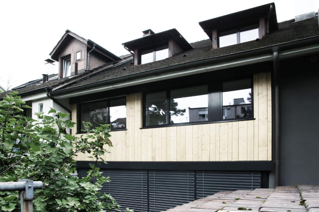 Umbau von KGRUPPE Architekten Basel - Mehrfamilienhaus mit Holzverkleidung und Dachbodenfenstern.