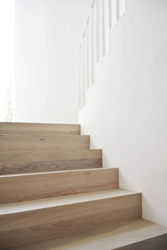 von KGRUPPE Architekten Basel - Eine Treppe aus hellem Holz in einem minimalistischen, weissen Innenraum.