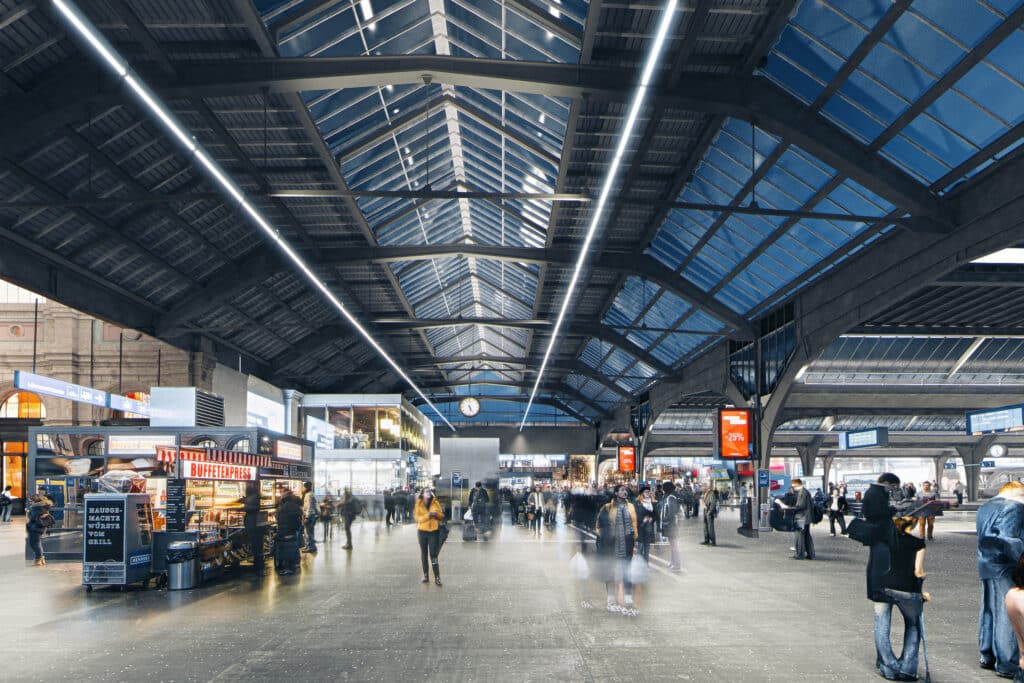 von KGRUPPE Architekten Basel - Ein belebter Bahnhof mit hohen Glasdachstrukturen und Menschen, die sich bewegen oder an Ständen stehen. Digitaluhren und Werbeschilder sind sichtbar.