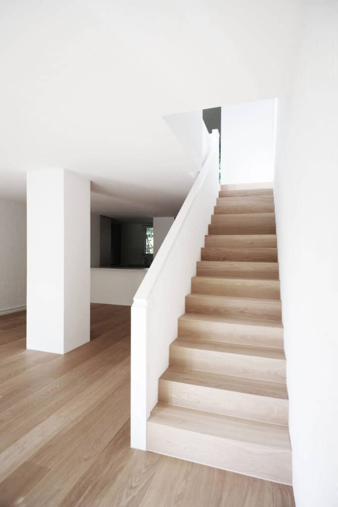 von KGRUPPE Architekten Basel - Holztreppe in modernem, minimalistischen Innenraum mit weiss gestrichenen Wänden und Holzboden.