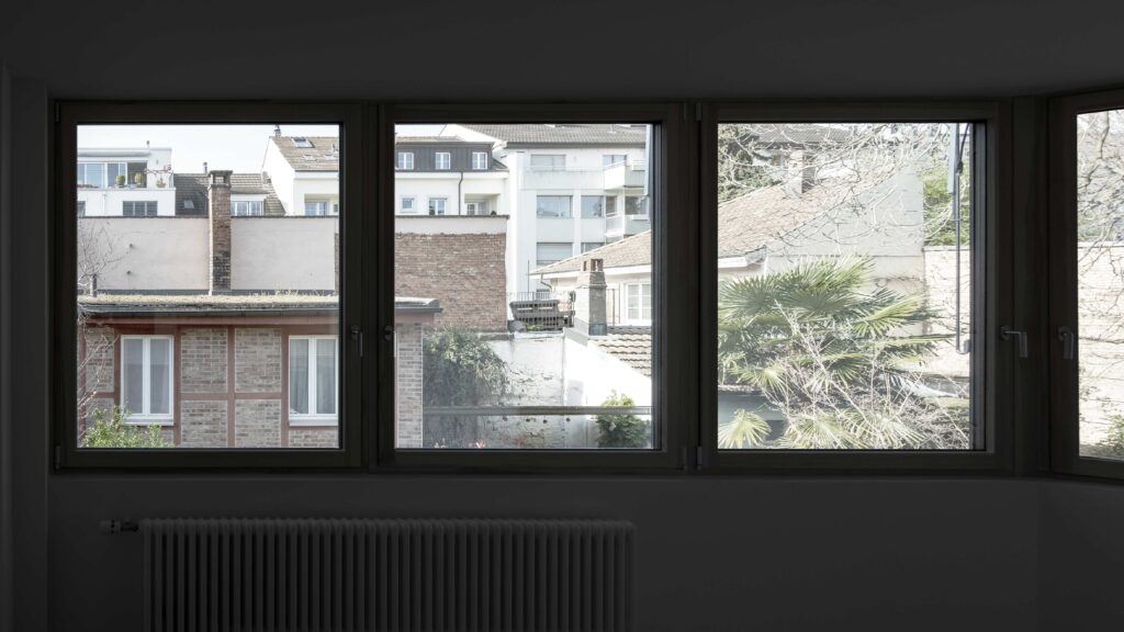 Umbau von KGRUPPE Architekten Basel - Blick aus einem Fenster auf eine Wohngegend mit mehrstöckigen Gebäuden und Palmen im Vordergrund.